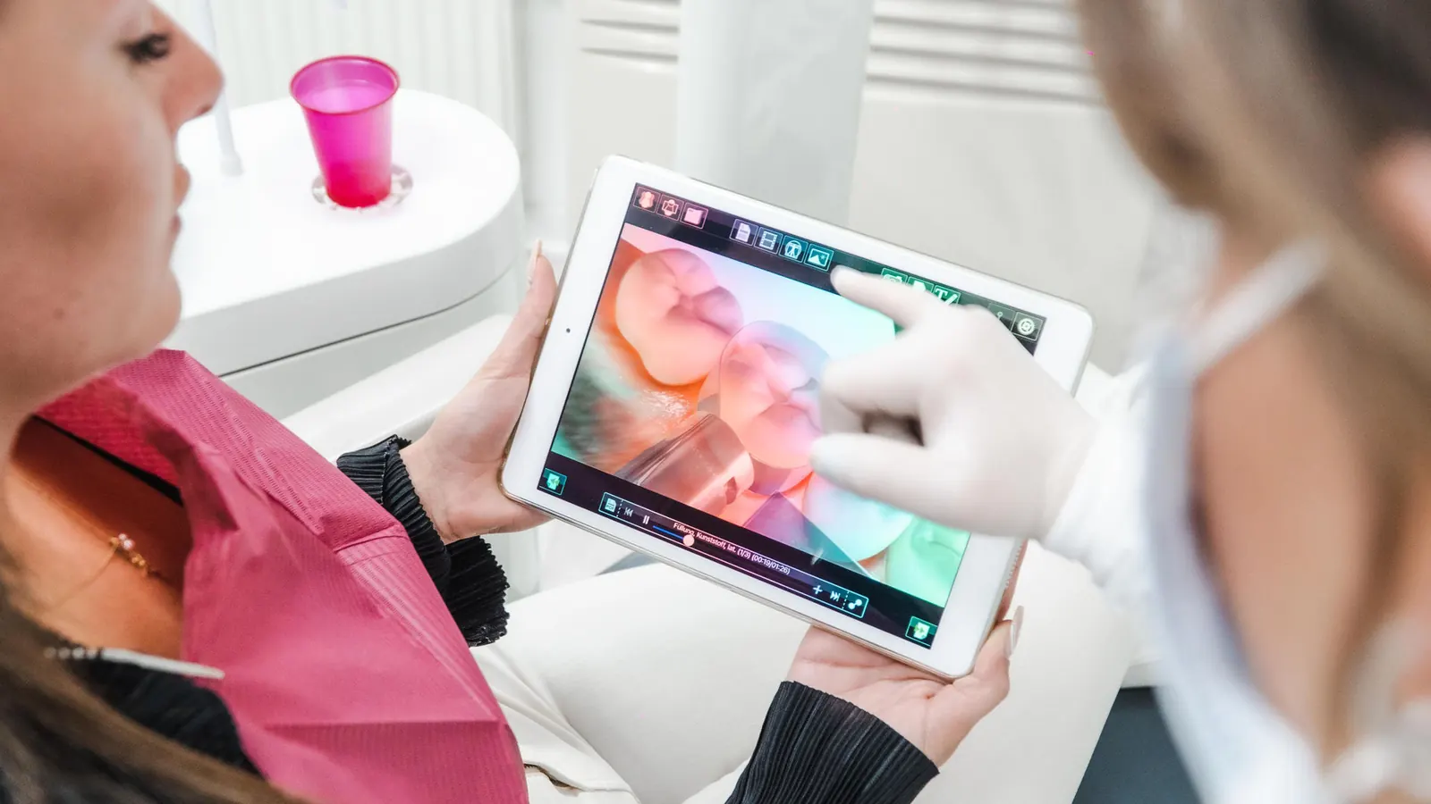 Zahnärztin zeigt einer Patientin die Darstellung ihrer Zähne auf einem Tablet
